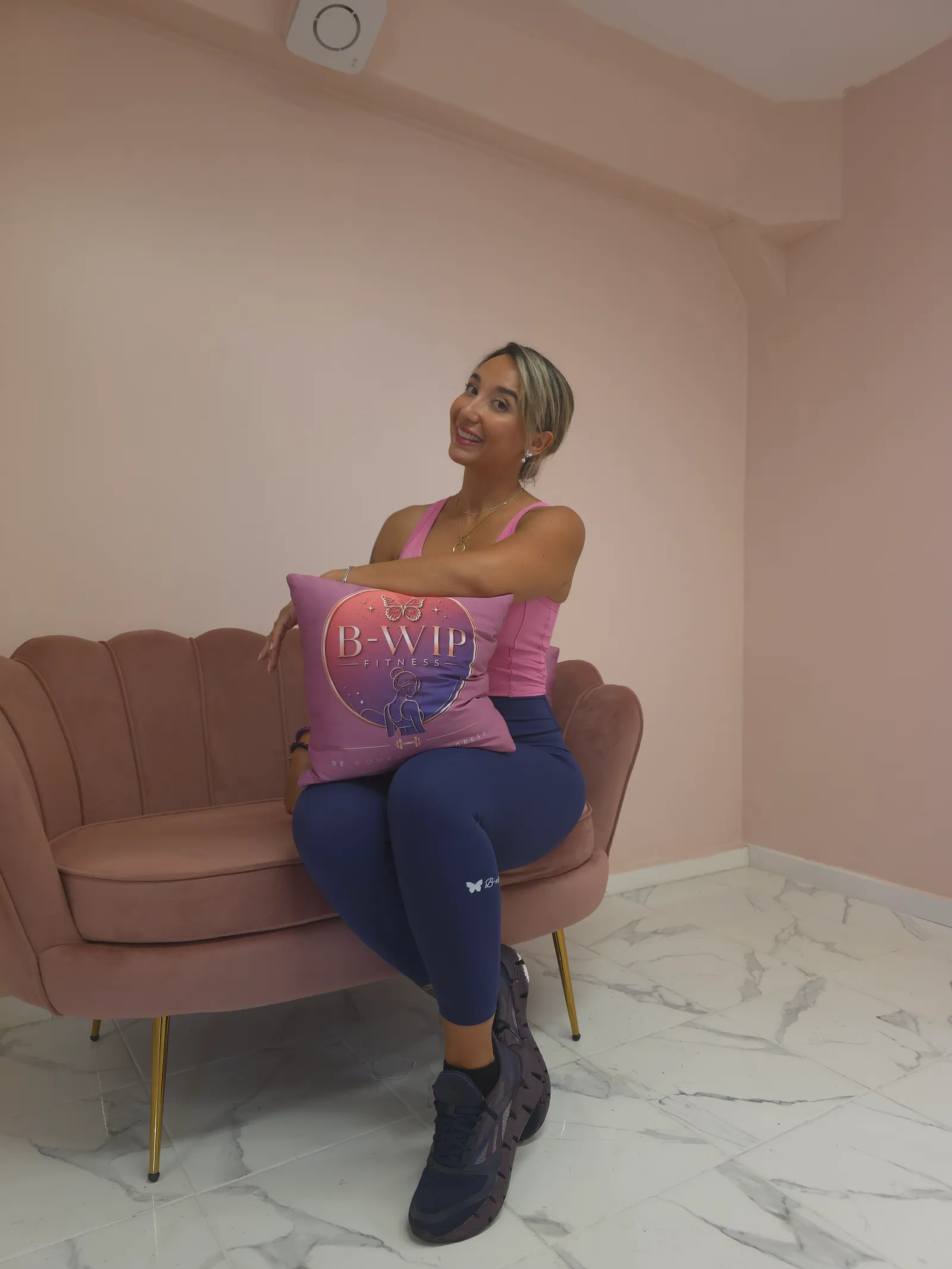 Une femme assise dans un fauteuil rose avec un coussin B-WIP Fitness