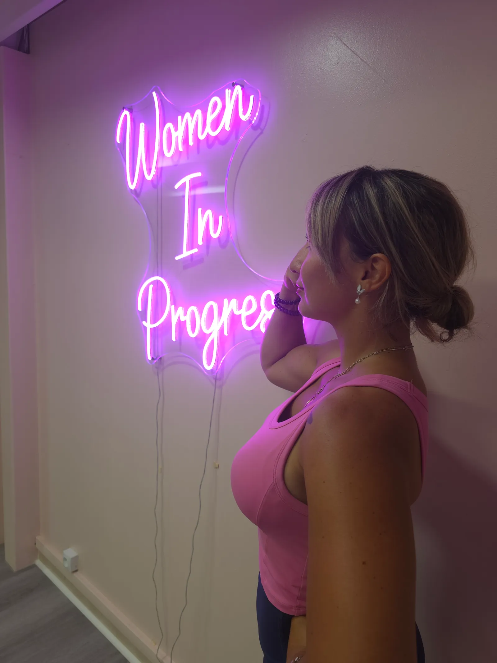 Une femme de profil devant le néon « Women In Progress » de B-WIP Fitness