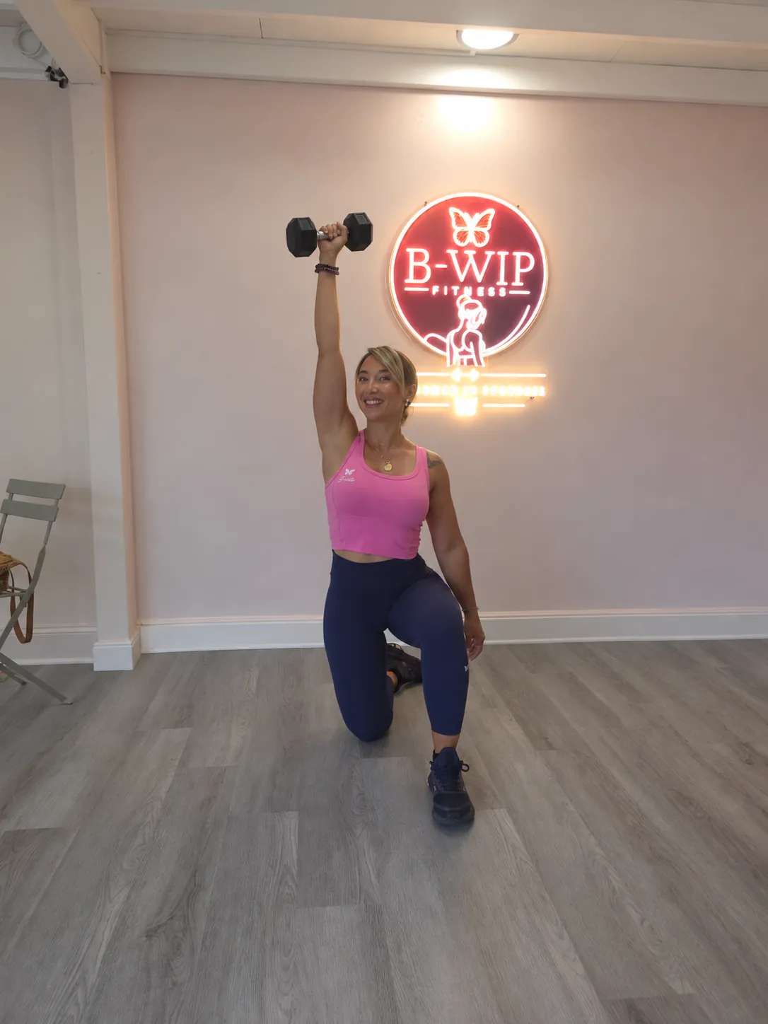 Une femme en fente, un haltère levé, devant le logo B-WIP Fitness