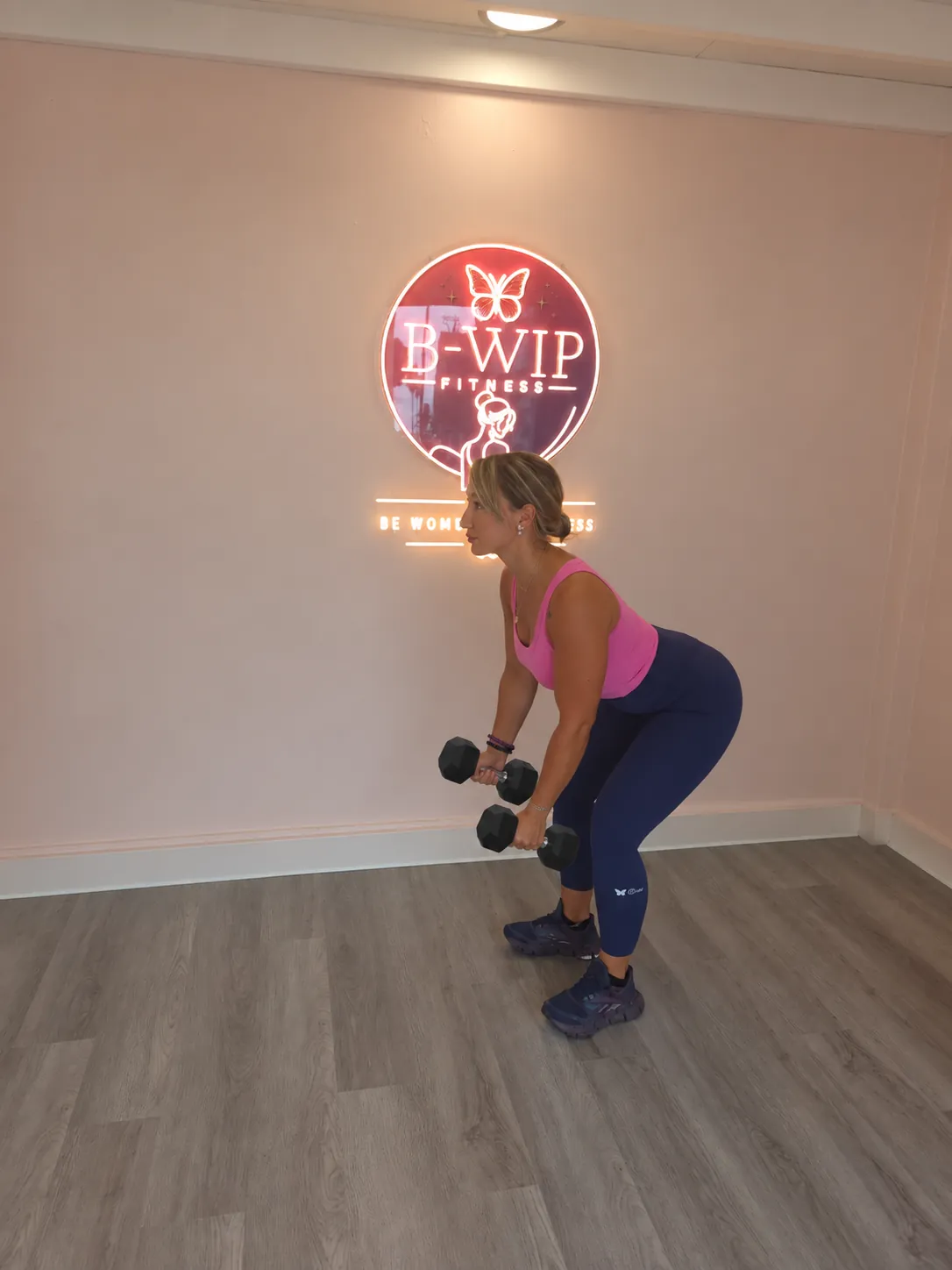 Une femme s'entraîne avec des haltères devant le logo B-WIP Fitness